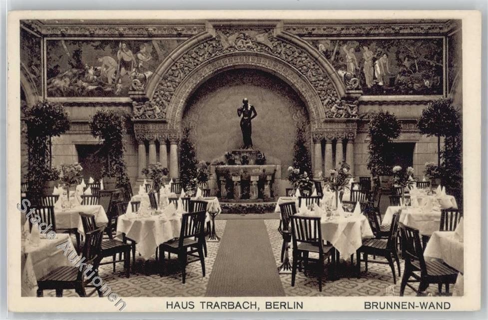 Schwarz-weiß-Foto eines alten Berliner Restaurant-Interieurs mit Tischen, die mit Vasen, einer Statue im Hintergrund, skulptierten Wänden und Pflanzen gedeckt sind.