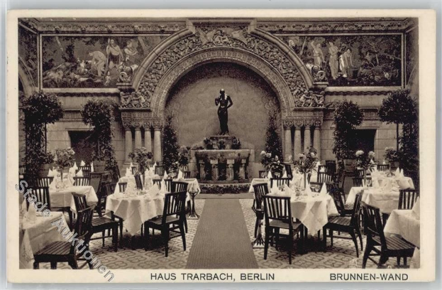 Schwarz-weiß-Foto eines alten Berliner Restaurant-Interieurs mit Tischen, die mit Vasen, einer Statue im Hintergrund, skulptierten Wänden und Pflanzen gedeckt sind.
