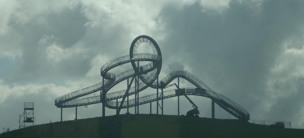 Eine Achterbahn auf dem Gipfel eines Hügels unter einem bewölkten Himmel, umgeben von Stützstrukturen.