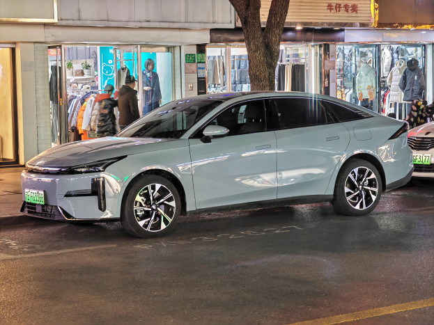 Ein Mitsubishi Lancer EV Elektroauto auf der Straße bei Nacht geparkt, umgeben von Gebäuden, Geschäften, Schaufensterpuppen, Schildern und Lichtern.