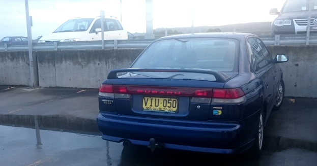 Verschiedene Autos und Pfosten sind zu sehen, wobei ein Auto ein gelbes Nummernschild mit Text darauf hat.