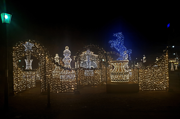 Ein Park bei Nacht mit Weihnachtslichtern in dekorativer Anordnung, beleuchtet von einer Straßenlaterne links.