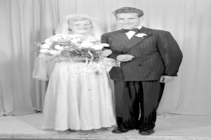 Ein Mann und eine Frau stehen nebeneinander auf einer Bühne, lächeln und die Frau hält einen Blumenstrauß, und ein Vorhang hinter ihnen.