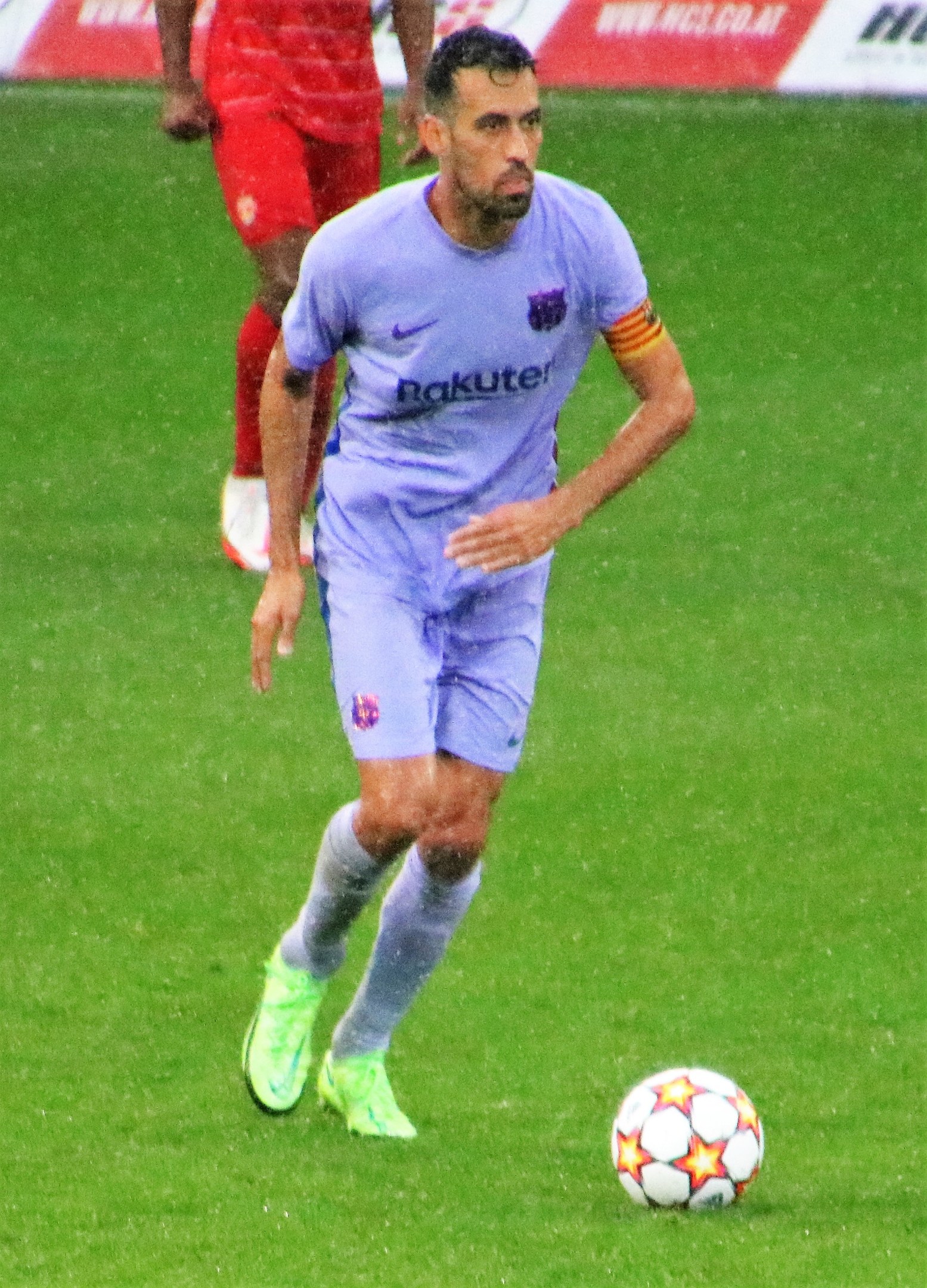 Fußballspieler in Bewegung auf einem Feld, der einen Sportdress und Fußballschuhe trägt, mit einer Tafel im Hintergrund.