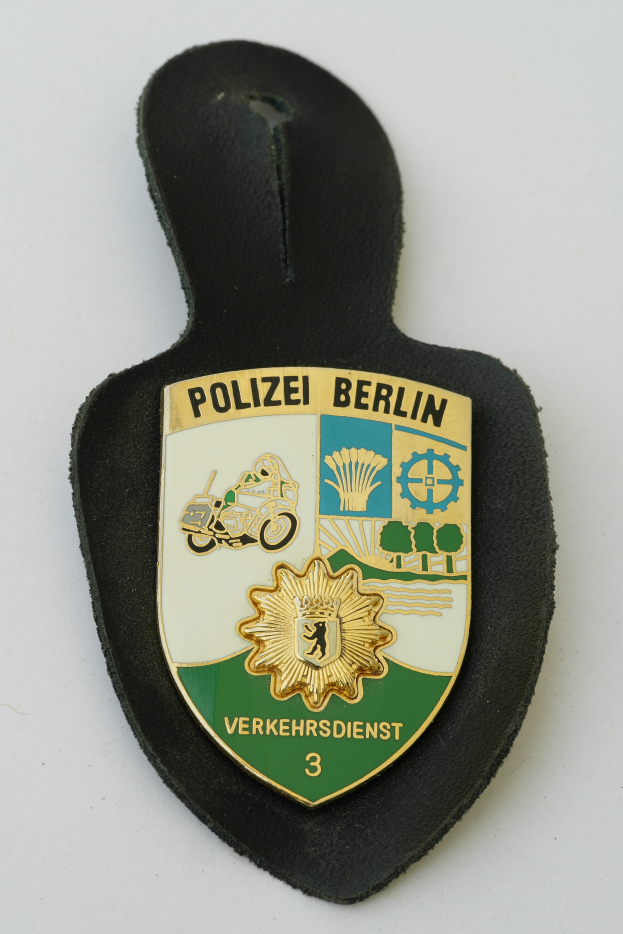 Ein Polizeischild mit der Aufschrift "Polizei Berlin" in fetter schwarzer Schrift auf einem blauen Schild mit einem weißen Stern und Rahmen.
