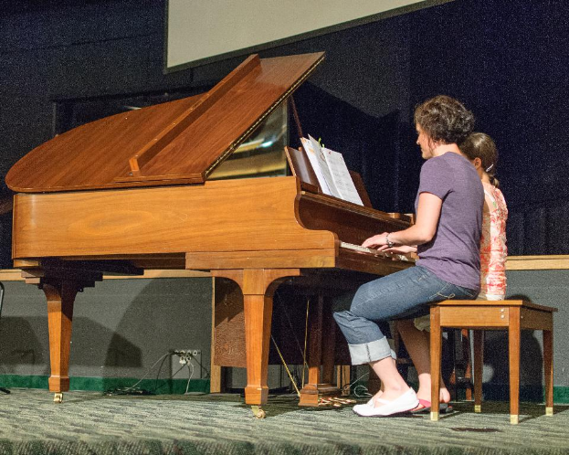 Eine Person, die auf einem Piano sitzt, mit einem Buch darauf, und eine Tür und Wand im Hintergrund.