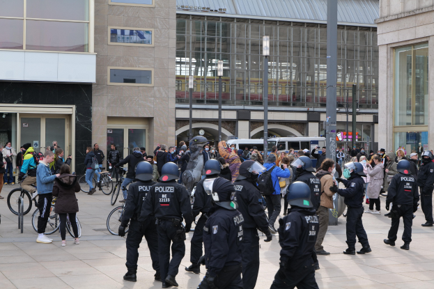 Polizisten mit Helmen vor einer Menge mit Fahrrädern, mit Glasfrontgebäuden, Laternen und Fahrzeugen im Hintergrund.