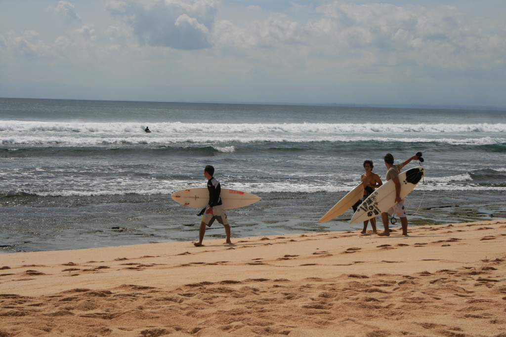 Drei Personen mit Ruderbooten auf sandigem Strand nahe dem Meer