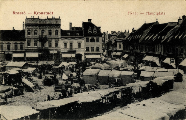 Schwarzes und weißes Foto eines belebten Marktes in Kronstadt, Deutschland mit Menschen, Zelten und Gebäuden unter einem sichtbaren Himmel.