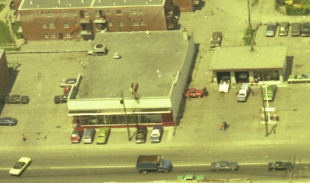 Eine Luftaufnahme einer Stadt mit zahlreichen Autos, die um Gebäude herum geparkt sind und einige Autos auf den Straßen fahren.