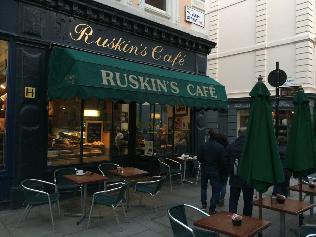 Eine Gruppe von Menschen vor einem Cafe mit der Aufschrift 'Ruskins Cafe'.