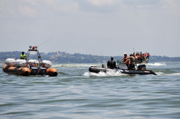 Eine Gruppe von Menschen, einige mit Helmen und Schutzausrüstung, befindet sich auf einem Boot im Wasser und ist von Bäumen und Gebäuden unter einem klaren blauen Himmel umgeben.