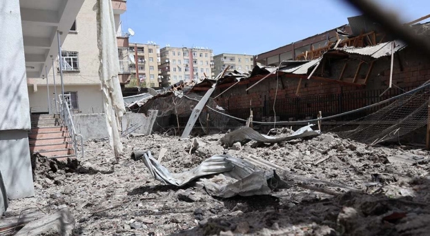Die Auswirkungen eines israelischen Luftangriffs in Gaza-Stadt, der die Trümmer eines zerstörten Gebäudes in der Mitte einer Straße zeigt, mit eingestürzten Wänden, Metallstangen, einem Zaun, einer Treppe, benachbarten Gebäuden mit Fenstern, einigen Bäumen und einem bewölkten Himmel.