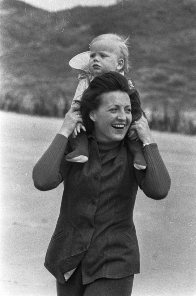 Eine Frau mit warmem Lächeln, die ein Baby hält, vor einem sanft unscharfen Hintergrund, der einen träumerischen Effekt erzeugt.