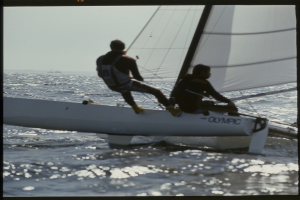 Zwei Männer auf einem Segelboot, das über das Wasser gleitet, mit dem Himmel im Hintergrund.