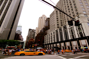 Eine Stadtansicht mit Gebäuden, Ampeln, Fenstern, einigen Fußgängern, Autos und Himmel.