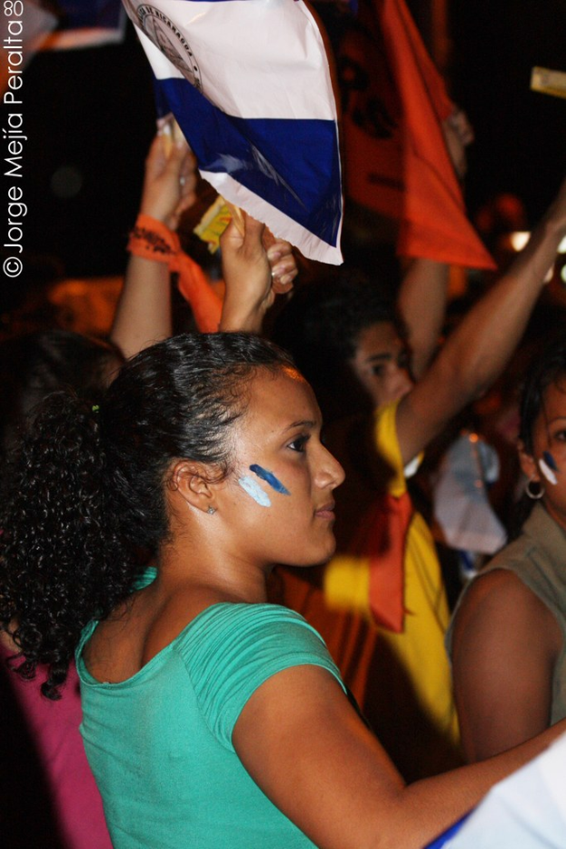 Frauen in grünen T-Shirts bei einer Demonstration, die weiße Schilder in den Händen halten, mit vielen anderen Mädchen hinter ihnen.