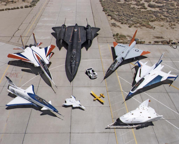 Ein Jet-Flug ist im Bildzentrum zu sehen, darunter eine Start- und Landebahn und Büsche im Hintergrund.