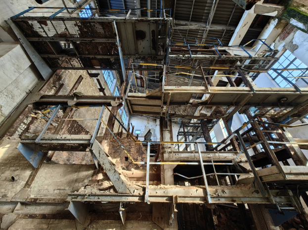 Alter Industriebau mit zentralem Metallgerüst, umgeben von verrosteten Eisenstangen, Treppen, Wänden und Fenstern, zeigt Anzeichen von Verfall und Verfall.