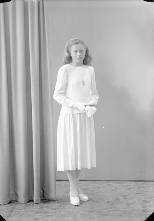 Ein junges Mädchen in einem weißen Kleid steht vor einem Vorhang, mit Schuhen bekleidet, bereit für eine Vorstellung.