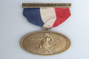 Eine goldene Medaille mit einer roten, weißen und blauen Schleife, die mit "Championship" beschriftet ist und ein Bild einer Person zeigt.
