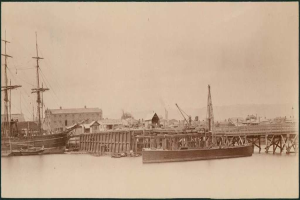 Eine Szene mit Wasser, Booten, Gebäuden, Strommasten, und einem Himmel.