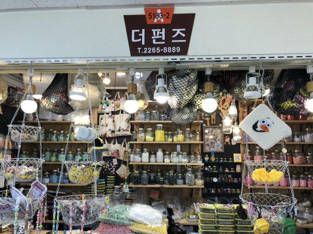 Ein unordentlicher Laden in Seoul, der verschiedene Gegenstände wie Körbe, Lampen, Flaschen und Spielzeuge auf Regalen ausstellt, mit einem Schild oben, das darauf hinweist, dass es einer der besten koreanischen Läden ist.