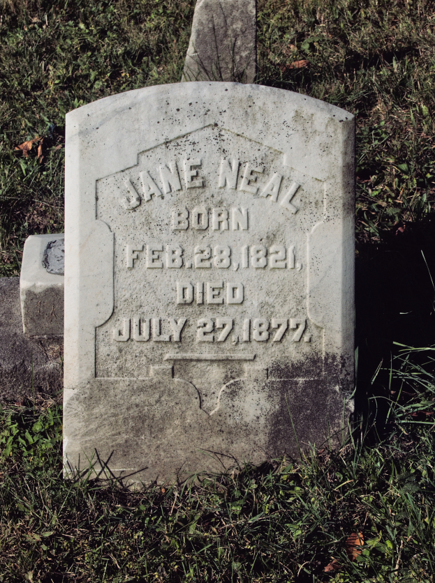 Ein Grabstein mit der Inschrift des Namens Jane Neal und ihrer Geburts- und Todestage, umgeben von Gras.