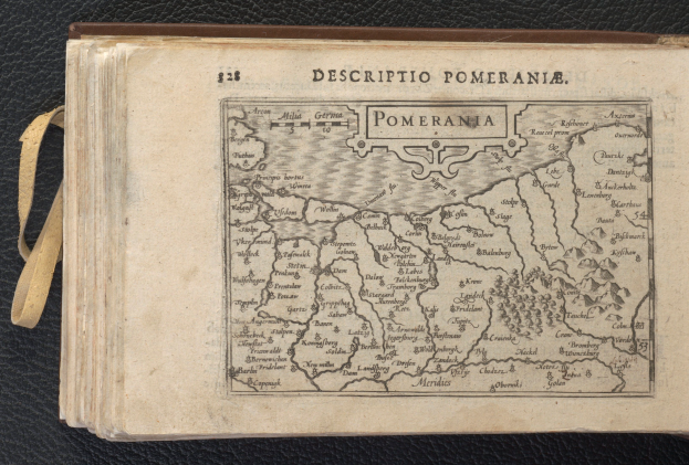 Ein altes Buch mit einer detaillierten Karte von Pommern, das verschiedene Städte und Ortschaften zeigt, liegt auf einer schwarzen Oberfläche.