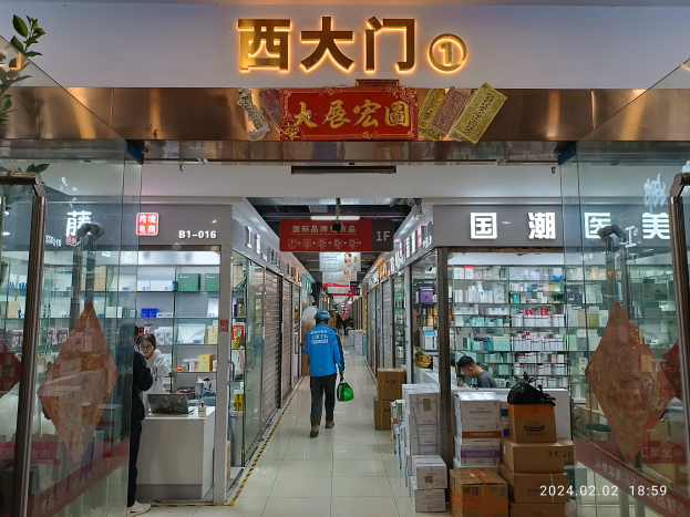 Innenansicht einer chinesischen Apotheke mit Glaswänden, Regalen voller Artikel, verstreuten Kartons auf dem Boden und einer Pflanze auf der linken Seite.