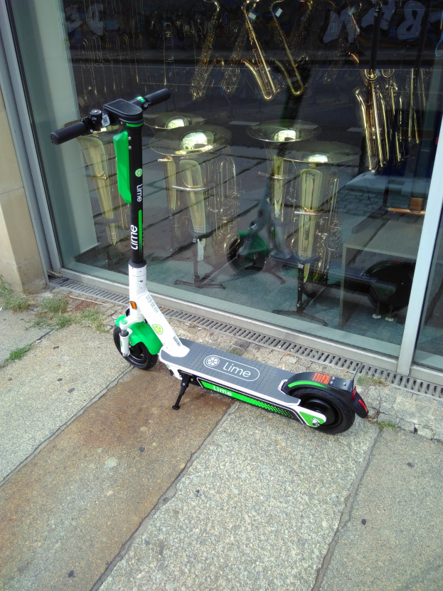 Elektro-Scooter auf einem Gehweg vor einem Laden mit einer Glasfront geparkt.