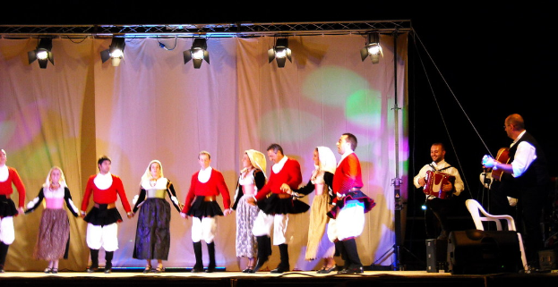 Ausführende auf der Bühne mit einem Vorhang im Hintergrund, Lichter oben, Musiker rechts und ein weißer Stuhl in der rechten unteren Ecke.