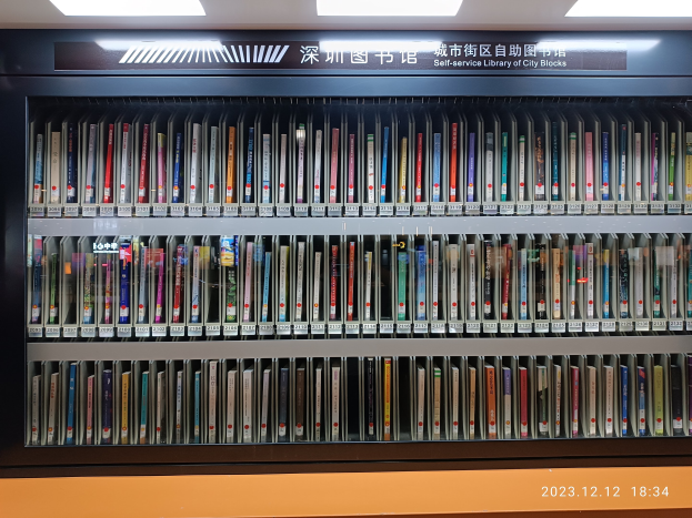 Eine gut beleuchtete Bibliothek mit hohen Bücherregalen voller Bücher, die ein Schild mit Text und ein Wasserzeichen am Boden zeigt, ähnelt einer Selbstbedienungsbibliothek der Stadtblöcke.