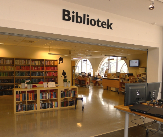 Mehrere Holzregale voller Bücher, mit Monitoren auf der rechten Seite und dem Wort "BIBLIOTECA" oben angezeigt.
