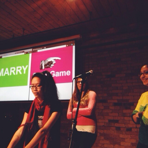 Drei Frauen, die nach links schauen, mit einem Mikrofonständer in der Mitte und einem Bildschirm mit Text auf der linken Seite.