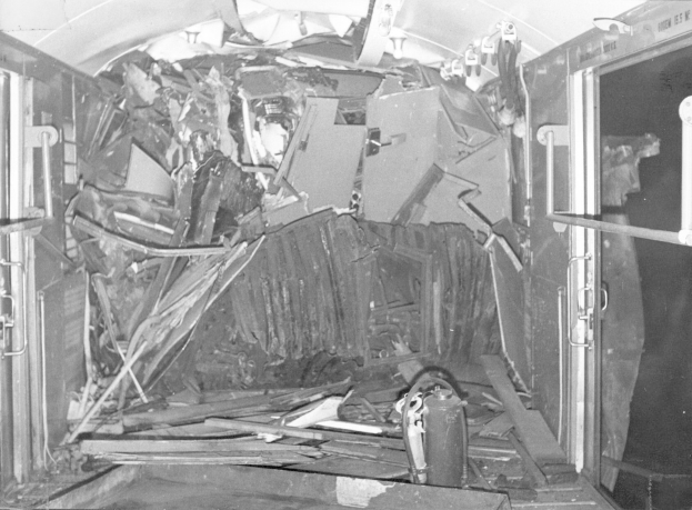 Schwarz-weiß-Foto eines zerstörten Zuginnenraums mit verstreuten Metallstangen, Lampen und Trümmern.