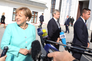 Bundeskanzlerin Angela Merkel spricht vor der Kanzleramt in Berlin mit Reportern, umgeben von einer Gruppe von Menschen, einige halten Mikrofone, mit Gebäuden mit Fenstern und Türen im Hintergrund.