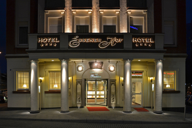 Das Essenerhof Hotel in Berlin, Deutschland, ein mehrstöckiges Gebäude mit Fenstern, Türen, Säulen und einem Namensschild, das entlang einer Straße mit Fahrzeugen auf der rechten Seite und einem sichtbaren Himmel liegt.