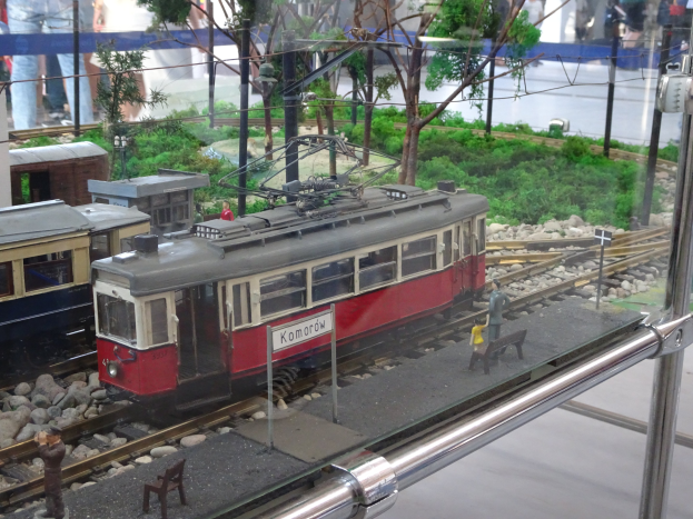 Modellbahnausstellung in einer Glasvitrine mit Miniatur-Eisenbahnlandschaft und Zuschauern.