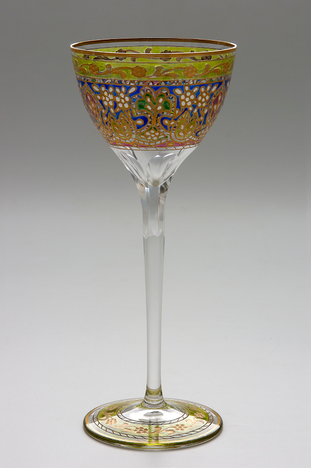 Ein Weinglas mit einem grünen und goldenen, detaillierten Design steht auf einer weißen Oberfläche und hat einen Stiel und eine schalenförmige Form mit einer breiten Basis und einem schmalen Hals.