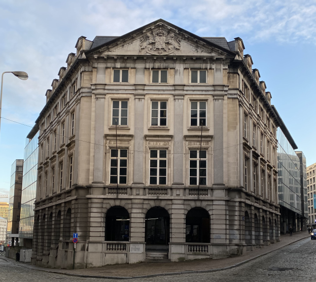 Das Deutsche-Bank-Gebäude in Frankfurt, ein großes Gebäude mit vielen Fenstern, umgeben von Straßenlaternen, Autos, Fußgängern und einem bewölkten Himmel.