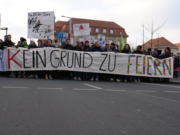 Demonstranten mit einem Transparent "Kein Grund zu Feiern" gegen deutsche Sparpolitik, mit Straßeninfrastruktur und Gebäuden im Hintergrund.