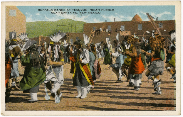 Eine Gruppe von Menschen in Kostümen hält Stöcke und tanzt vor Gebäuden, Hügeln und einem bewölkten Himmel, mit der Aufschrift "Buffalo Dance at Tesque Indian Pueblo near Santa Fe, New Mexico" oben.
