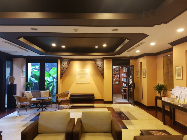 Eine Hotellobby mit Sitzbereichen mit Sofas und Stühlen, Tischen, Zimmerpflanzen, Bücherregalen, Deckenleuchten, Wanddekorationen und Seitentisch-Dekorationen, beleuchtet durch natürliches Licht von Fenstern und Türen.
