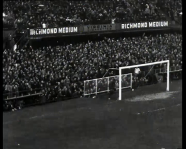Ein Schwarz-Weiß-Foto eines Fußballspiels in einem Stadion mit Zuschauern auf den Rängen und Spielern auf dem Feld, das ein Tor mit Netz und eine Anzeigetafel zeigt, auf der "West Ham United v West Ham United - FA Cup Final" steht.